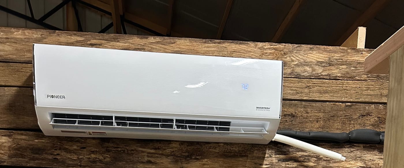 The heat pump mounted on the barn's warm wood-plank wall.